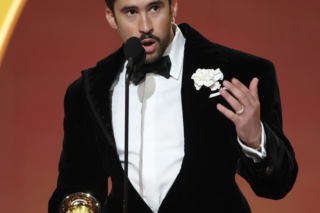 Bad Bunny accepts Album of the Year 2025 at the Grammy Awards while holding his trophy and speaking on stage.